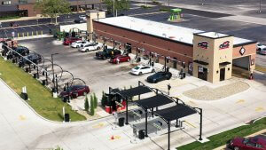 drone view of location caddy corner showing building tower with club car wash logo as closest corner and a parking lot full of cars to the left with green grass surrounding