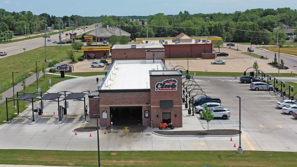 drone view of straight on building with club car wash logo in center, entry lanes to the left, and vacuums to the right surrounded with beautiful green grass