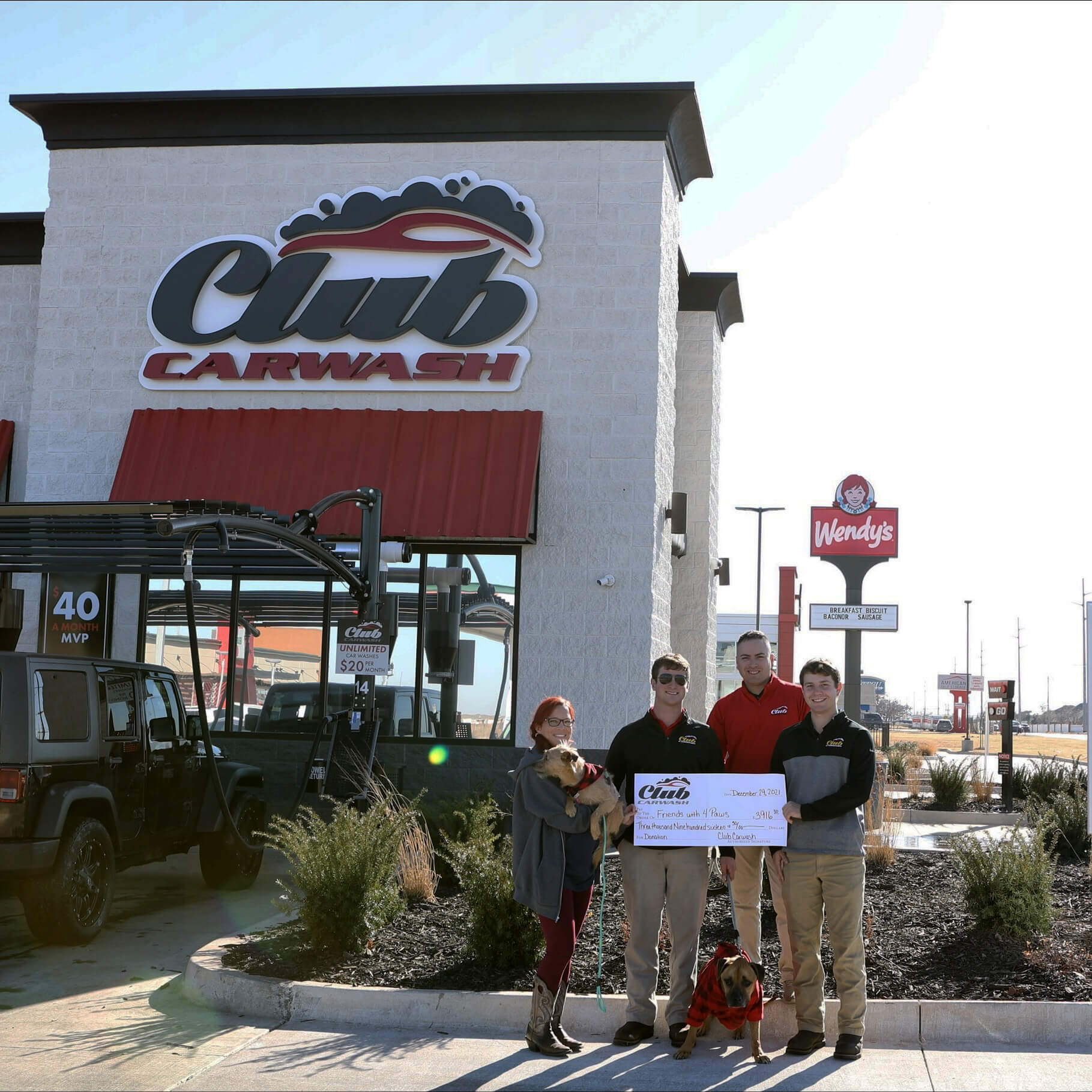 Club Car Wash employees holding a check with Friends with 4 Paws representatives in front of Club Car Wash.